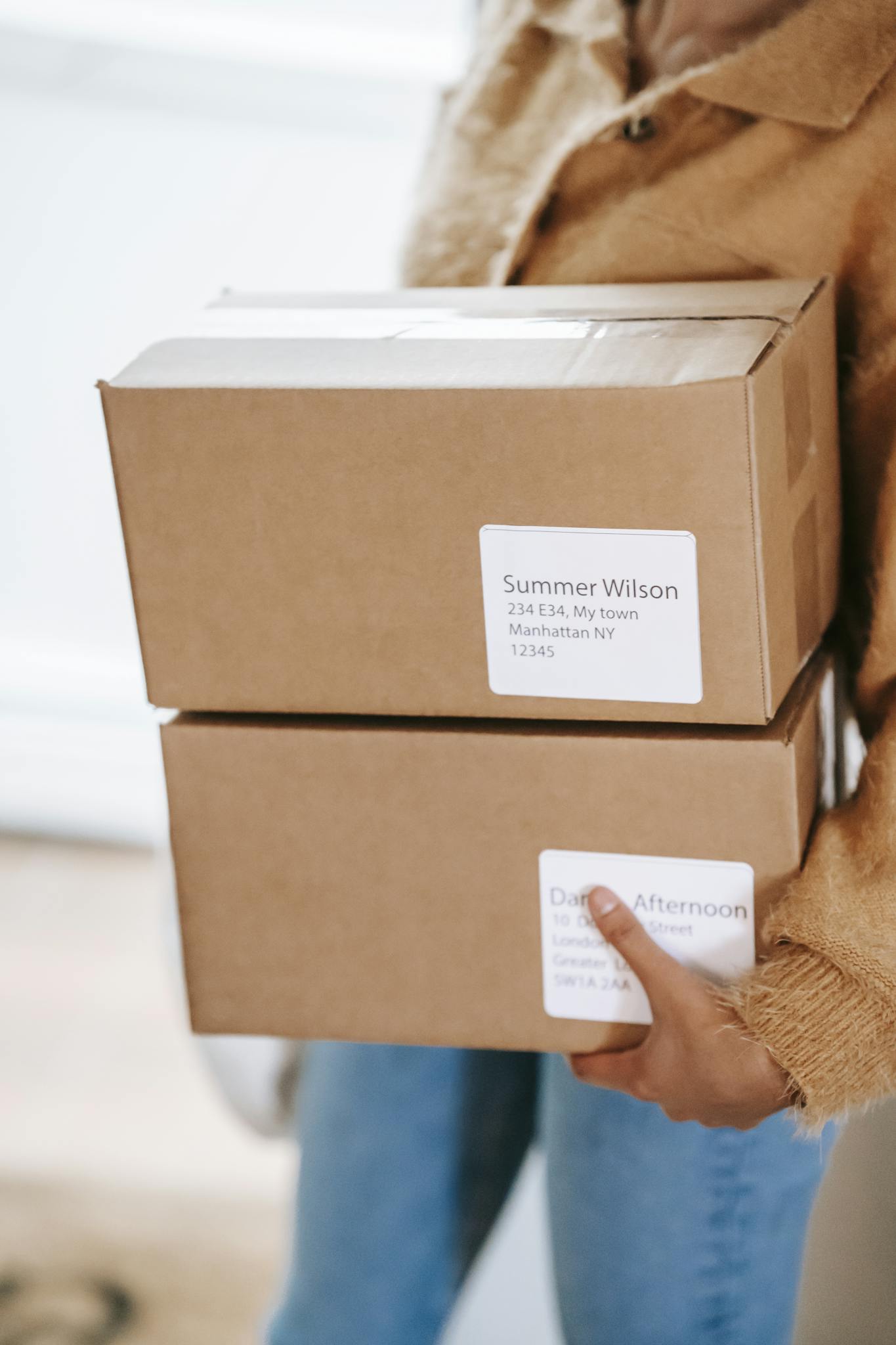 Woman holding cardboard boxes with shipping labels indoors, showcasing delivery service.