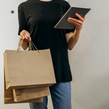 Woman in black shirt with shopping bags using a tablet at home, symbolizing online shopping convenience.