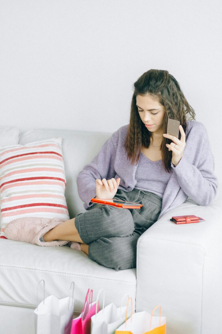 Woman sitting on a couch enjoying online shopping with a digital device and credit card.